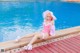 A woman in a pink bathing suit and hat sitting by a pool.