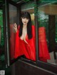 A woman in a red robe is looking out of a window.