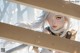 A woman with long white hair and golden armor peers through wooden slats.