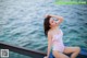 A woman in a white bathing suit sitting on a dock by the water.