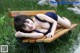 A woman laying on a wooden bench in the grass.